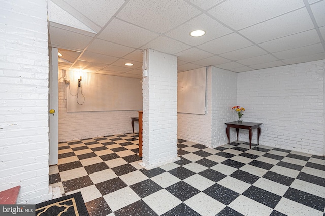 basement featuring brick wall and a drop ceiling