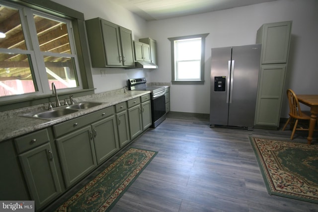 kitchen featuring under cabinet range hood, stainless steel appliances, a sink, green cabinets, and dark wood finished floors