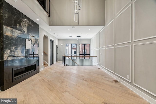 interior space with light wood-type flooring, a high end fireplace, and a high ceiling