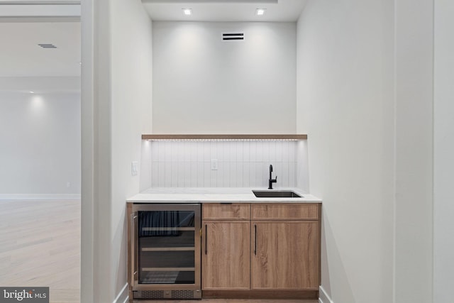 bar with light wood finished floors, beverage cooler, visible vents, a sink, and indoor wet bar