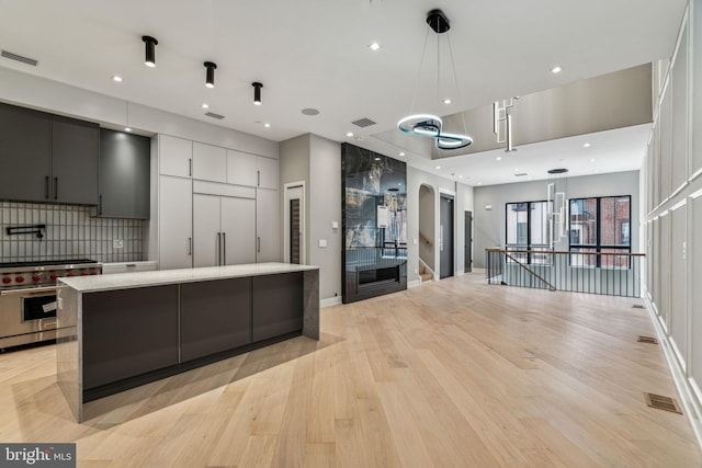 kitchen featuring high quality appliances, tasteful backsplash, light wood-type flooring, decorative light fixtures, and a large island