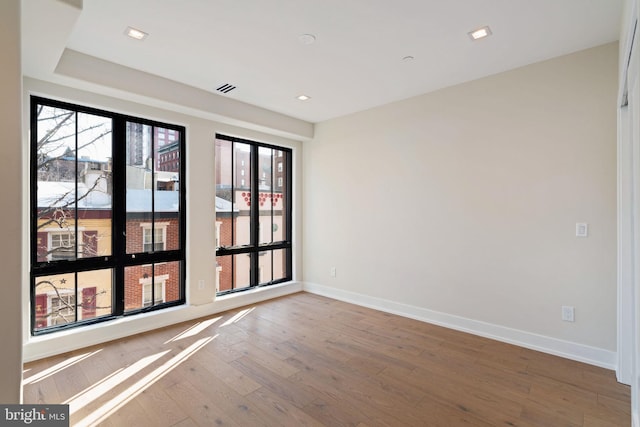 spare room featuring visible vents, plenty of natural light, baseboards, and wood finished floors