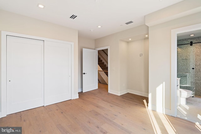 unfurnished bedroom featuring light wood-type flooring, ensuite bath, visible vents, and a closet