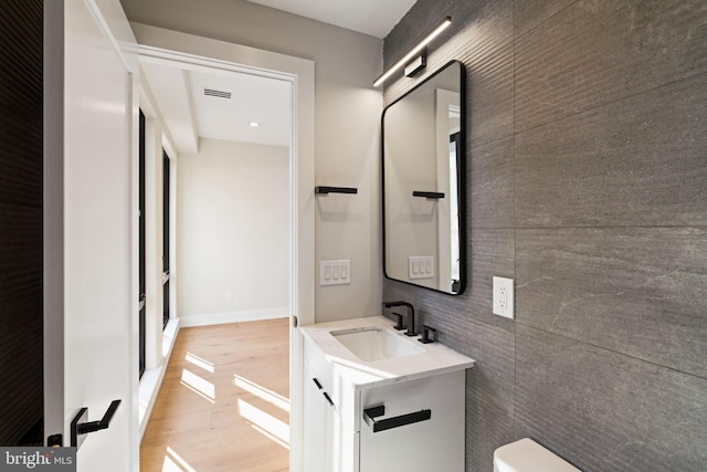 half bath with baseboards, visible vents, toilet, wood finished floors, and vanity