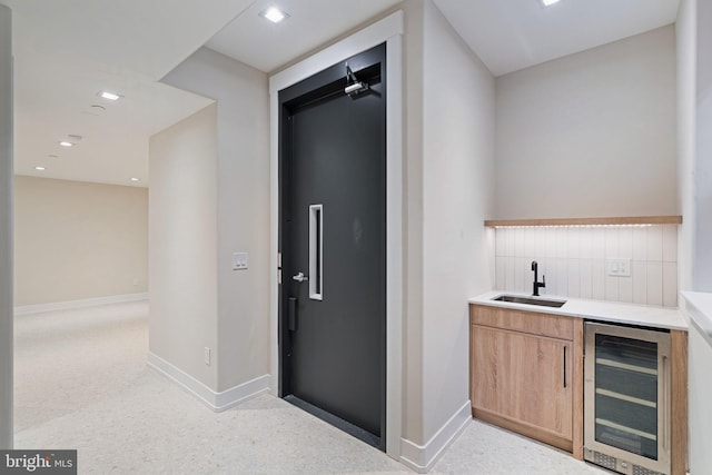 bar with tasteful backsplash, beverage cooler, a sink, and baseboards