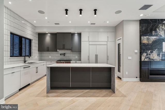 kitchen featuring light hardwood / wood-style floors, a center island, sink, white cabinets, and backsplash