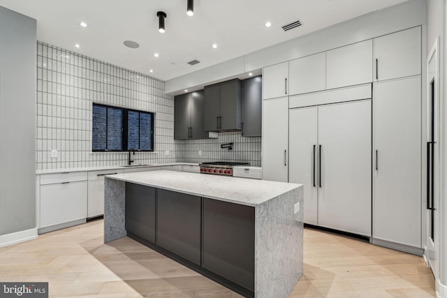 kitchen with a center island, tasteful backsplash, sink, white cabinetry, and light hardwood / wood-style flooring