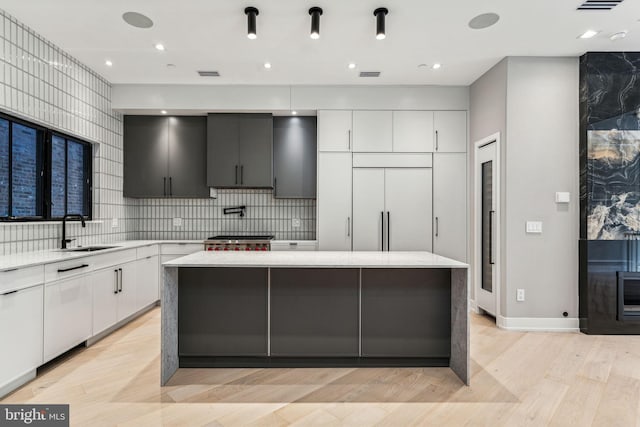 kitchen with a kitchen island, light wood-type flooring, sink, and white cabinetry