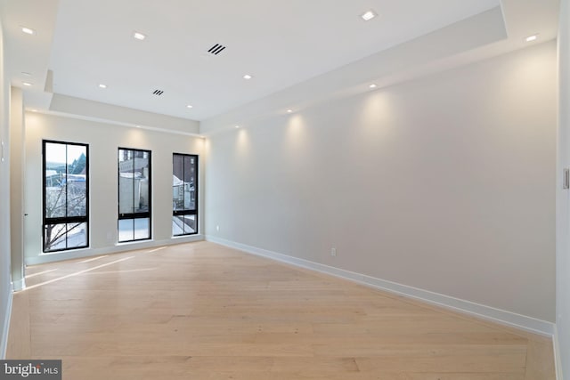 spare room featuring light wood finished floors, recessed lighting, a raised ceiling, visible vents, and baseboards