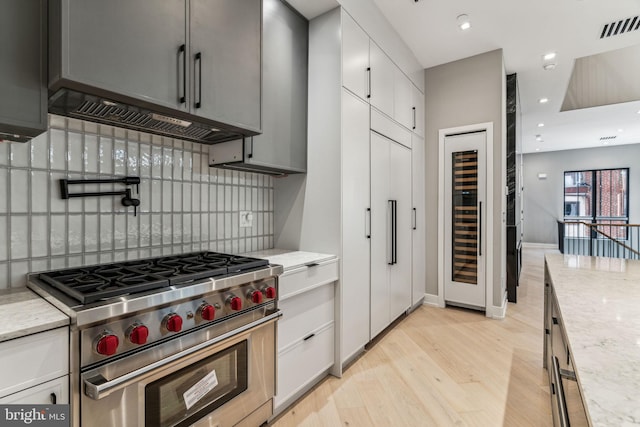 kitchen featuring light stone countertops, light wood-type flooring, luxury range, and tasteful backsplash