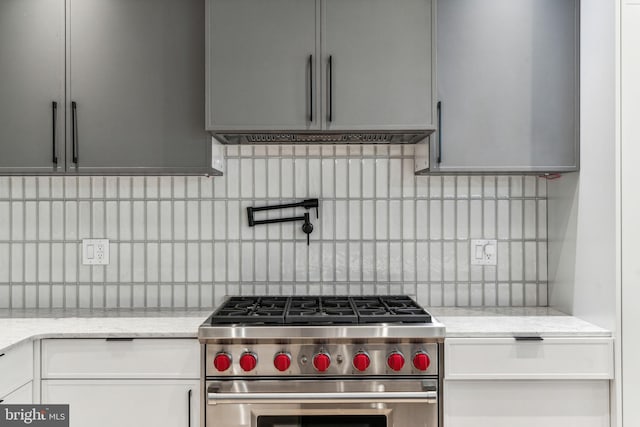 kitchen with gray cabinetry, high end stainless steel range oven, light stone counters, and tasteful backsplash