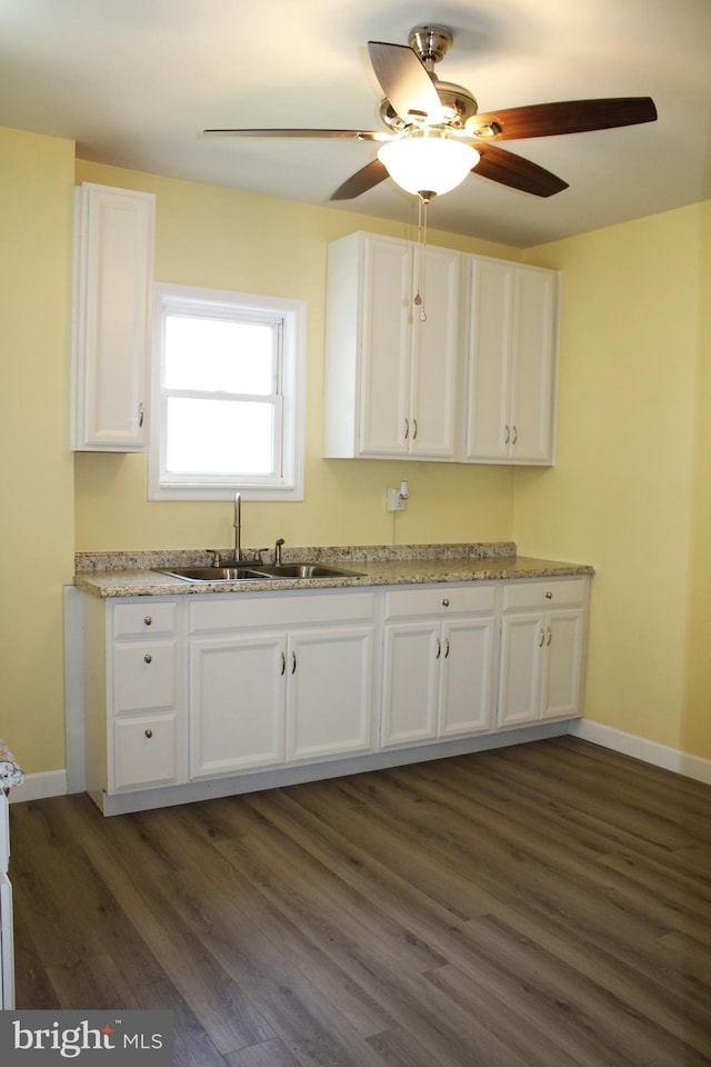 kitchen with dark wood-style flooring, white cabinetry, a sink, and baseboards