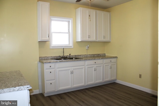 kitchen featuring dark wood-type flooring, white cabinetry, a sink, and baseboards