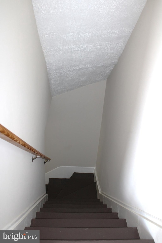 stairway featuring baseboards, vaulted ceiling, and a textured ceiling