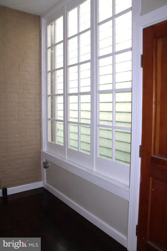 unfurnished room with dark wood-style floors, brick wall, and baseboards