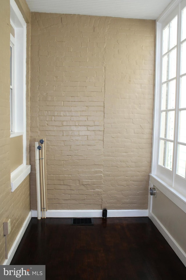 spare room featuring baseboards, brick wall, and wood finished floors