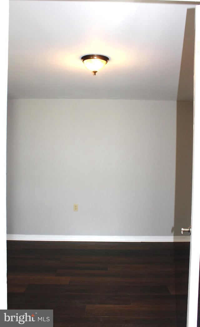 spare room with dark wood-style flooring and baseboards