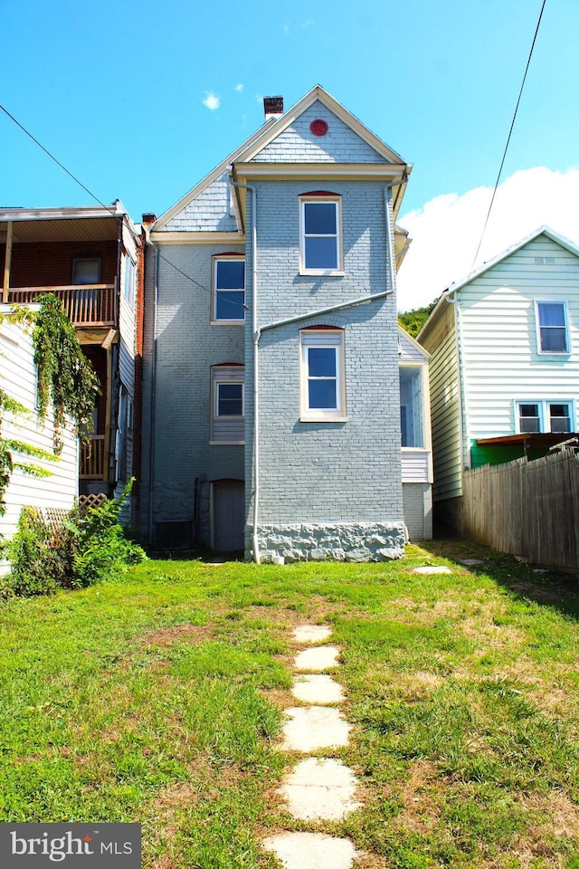 back of property with a chimney, fence, a lawn, and brick siding