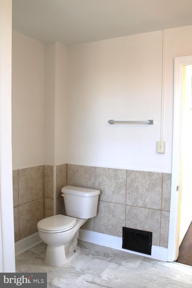 bathroom featuring visible vents, wainscoting, toilet, marble finish floor, and tile walls