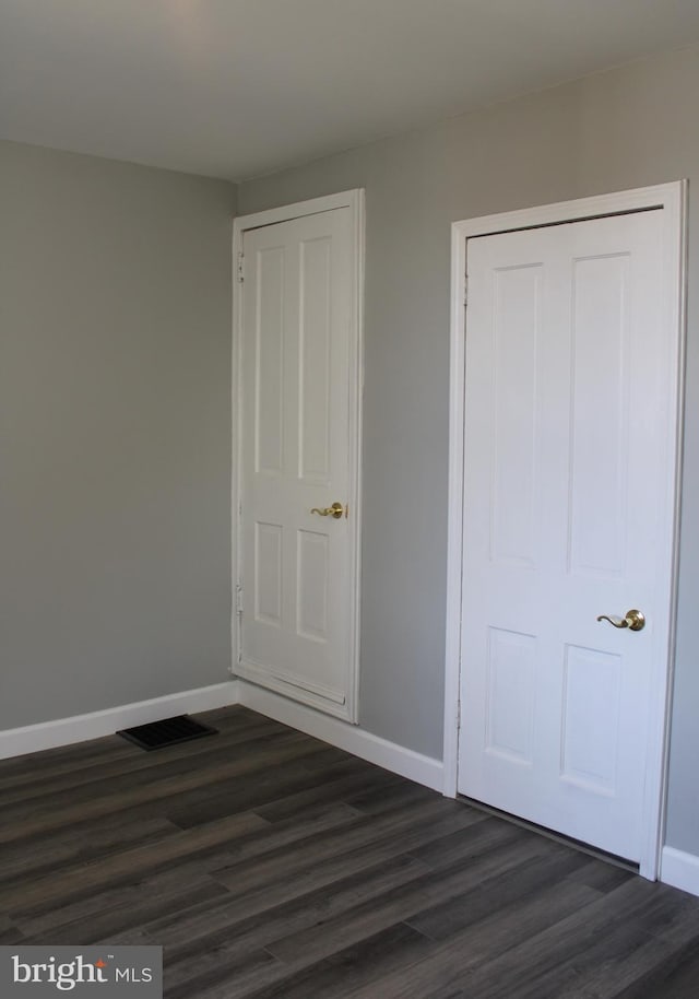 unfurnished bedroom featuring dark wood-style flooring, visible vents, and baseboards