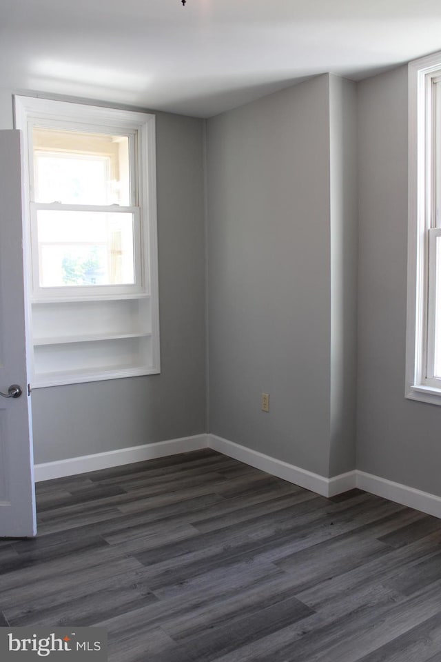 spare room featuring dark wood finished floors, a wealth of natural light, and baseboards