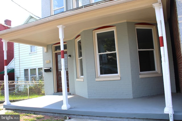 view of exterior entry with covered porch, fence, and brick siding