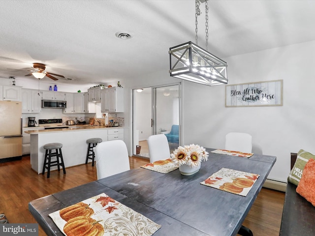 dining area with ceiling fan with notable chandelier, dark hardwood / wood-style floors, a baseboard heating unit, and a textured ceiling