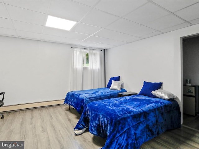 bedroom with a drop ceiling, a baseboard heating unit, and hardwood / wood-style flooring