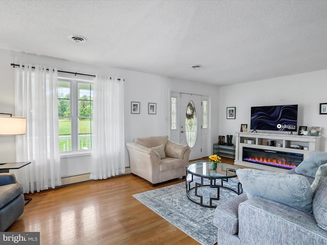 living room featuring light hardwood / wood-style floors, baseboard heating, and a textured ceiling