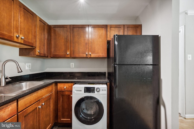 kitchen with freestanding refrigerator, a sink, washer / dryer, and brown cabinets