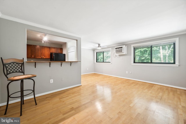 kitchen featuring light wood finished floors, brown cabinets, a kitchen breakfast bar, black refrigerator, and an AC wall unit