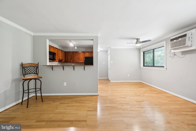 interior space with crown molding, a ceiling fan, an AC wall unit, light wood-type flooring, and baseboards