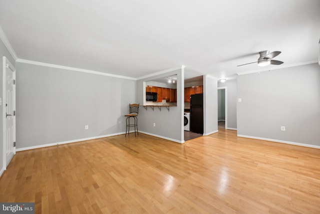 unfurnished living room featuring light wood-type flooring, washer / clothes dryer, crown molding, and baseboards