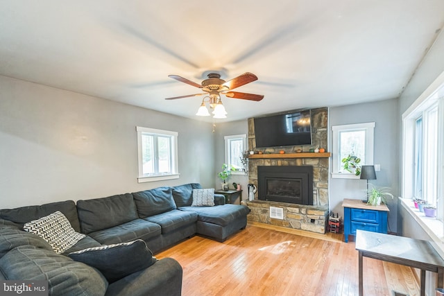 living room with light wood-type flooring, a healthy amount of sunlight, ceiling fan, and a stone fireplace