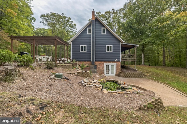 view of home's exterior featuring driveway, french doors, a chimney, a wooden deck, and a carport