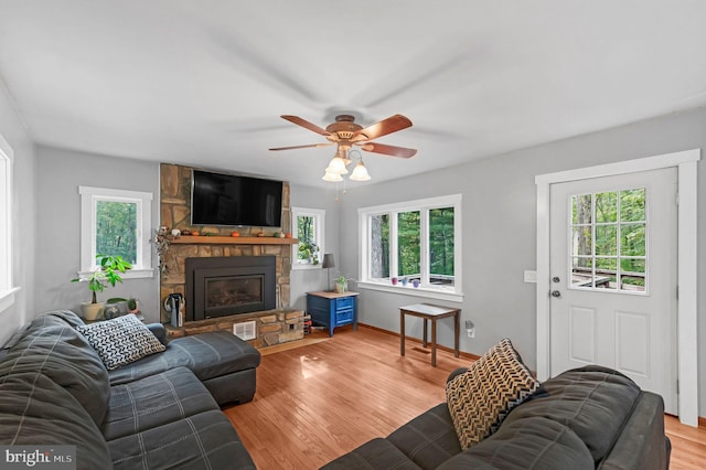 living area featuring a fireplace, visible vents, a ceiling fan, wood finished floors, and baseboards