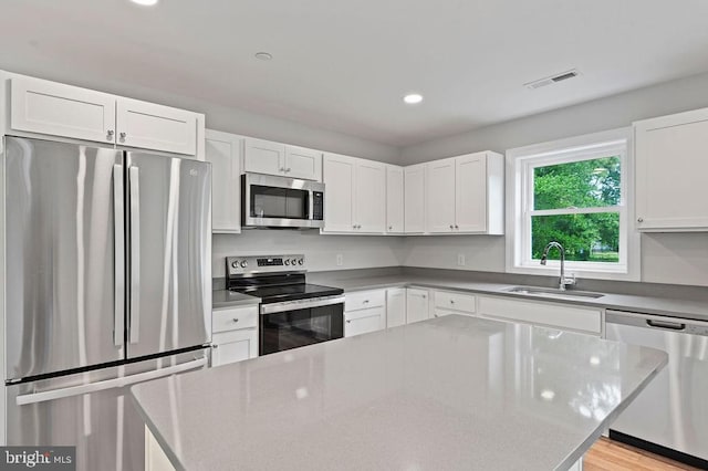 kitchen with appliances with stainless steel finishes, white cabinets, light wood-type flooring, a center island, and sink