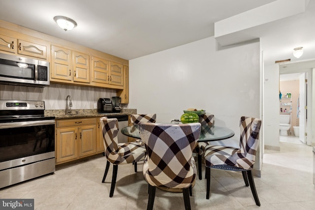 kitchen with light brown cabinetry, light tile patterned floors, stainless steel appliances, sink, and dark stone counters