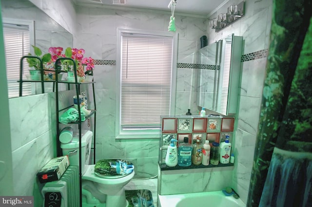 bathroom with a bathing tub, toilet, ornamental molding, and tile walls