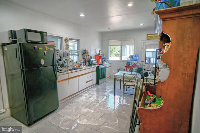 kitchen featuring white cabinetry, sink, light tile patterned floors, black fridge, and stainless steel range with electric cooktop