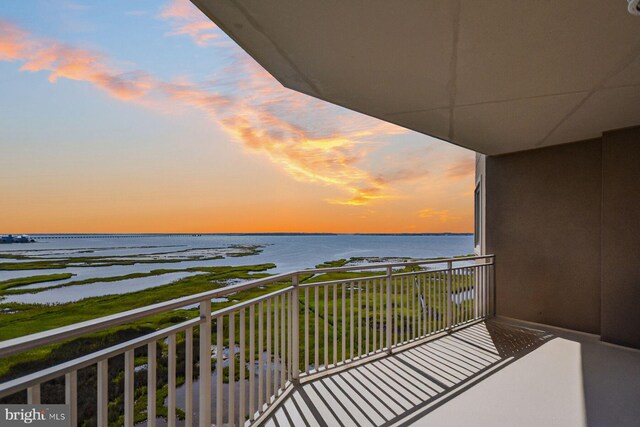 balcony at dusk featuring a water view