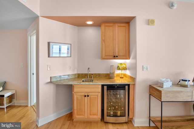 interior space with beverage cooler, light stone countertops, light hardwood / wood-style floors, and sink