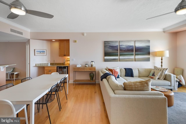 living room with ceiling fan, ornamental molding, beverage cooler, and light hardwood / wood-style floors