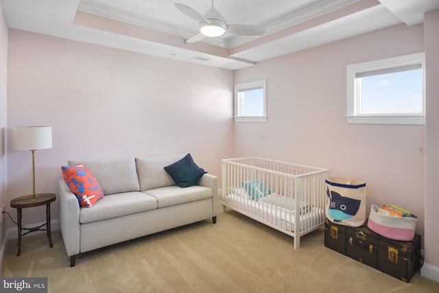 carpeted bedroom with a tray ceiling, a nursery area, crown molding, and ceiling fan