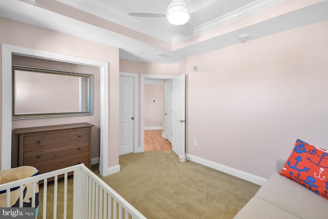 bedroom with a tray ceiling, a nursery area, ceiling fan, and light colored carpet