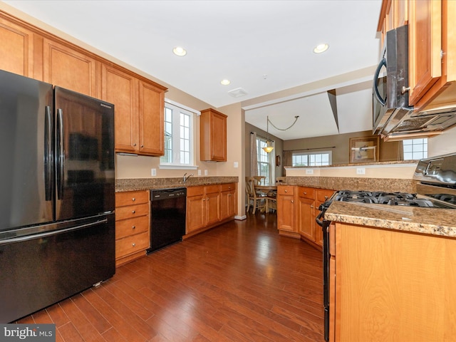 kitchen with hanging light fixtures, kitchen peninsula, dark hardwood / wood-style flooring, light stone countertops, and black appliances