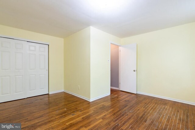 unfurnished bedroom featuring dark wood-type flooring, a closet, and baseboards