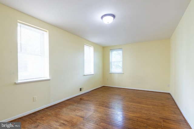 unfurnished room with wood finished floors, visible vents, and baseboards