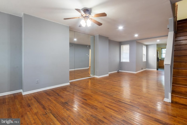 empty room featuring stairway, wood finished floors, a ceiling fan, and baseboards