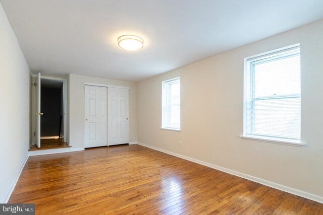 unfurnished bedroom featuring hardwood / wood-style floors, a closet, and multiple windows